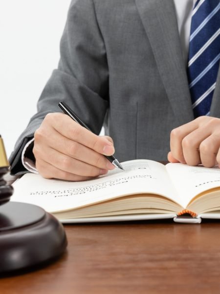 closeup-shot-person-writing-book-with-gavel-table-1-scaled.jpg